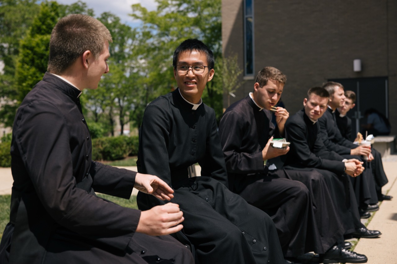 Seminarians in cassocks talking together outdoors on campus
